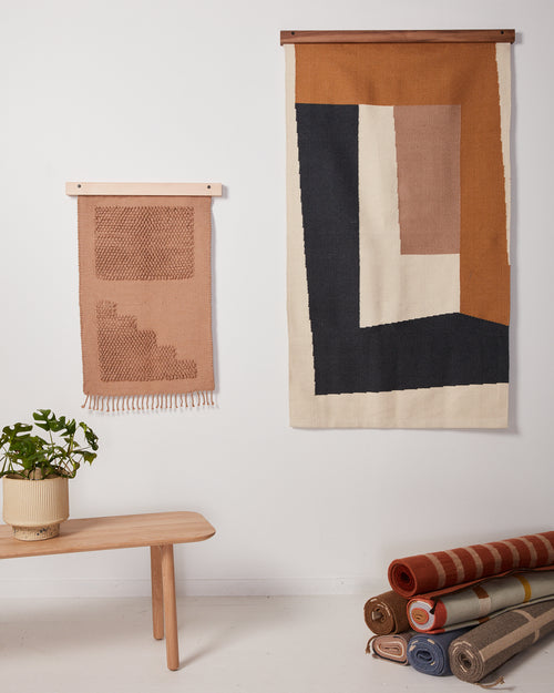 two rug hangers in walnut and maple holding MINNA minimal handwoven graphic rugs as wall art for home decor 
