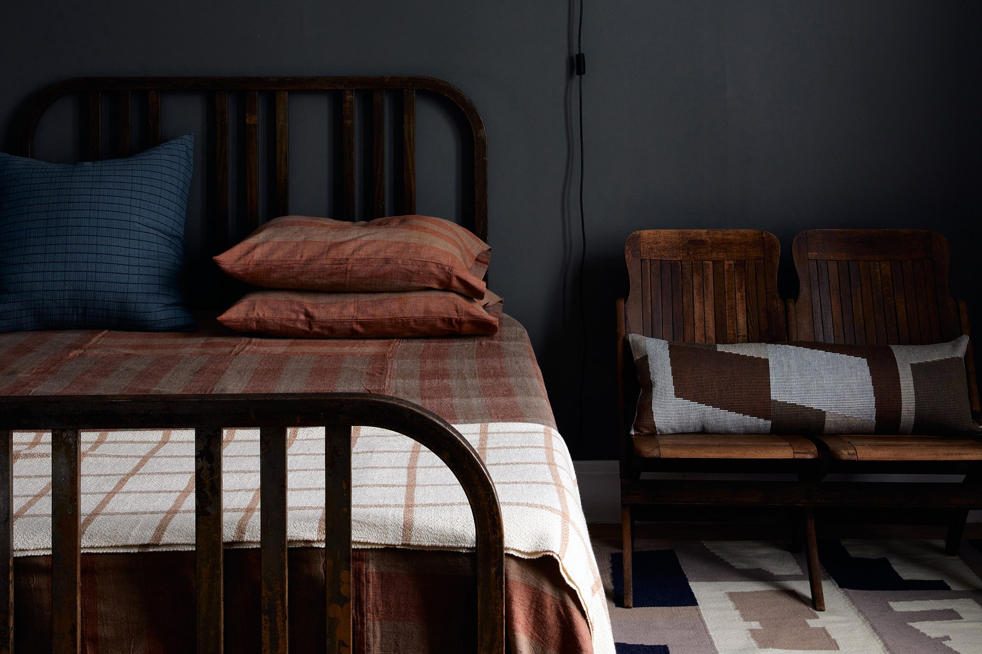 Bedroom with dark painted walls and ethically handwoven bedding, blankets, and rugs by MINNA. Rust, Navy, Camel, Neutral