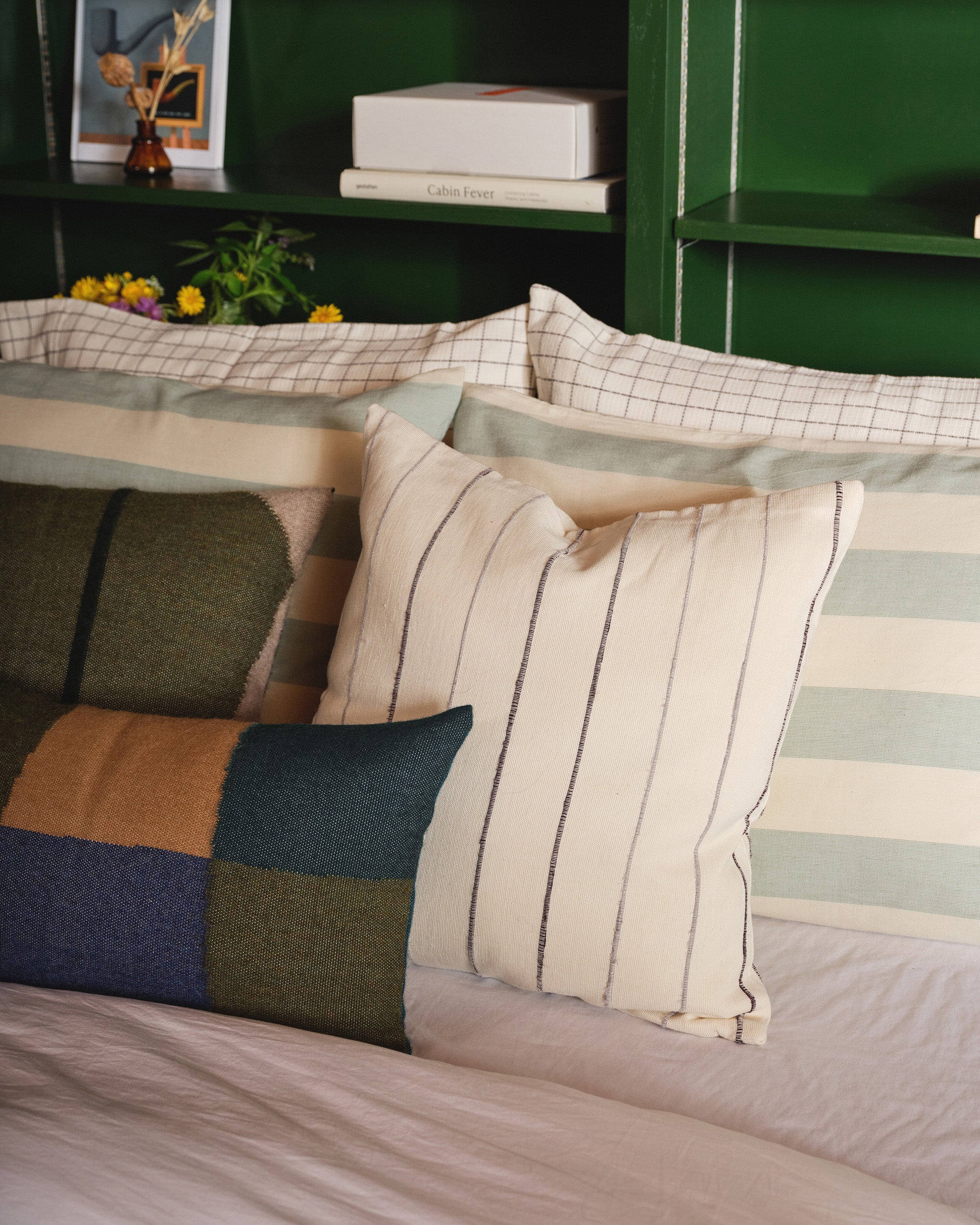 Ethically handwoven decorative throw pillows on a guest bed. MINNA patchwork and julie pillow in Hunter.