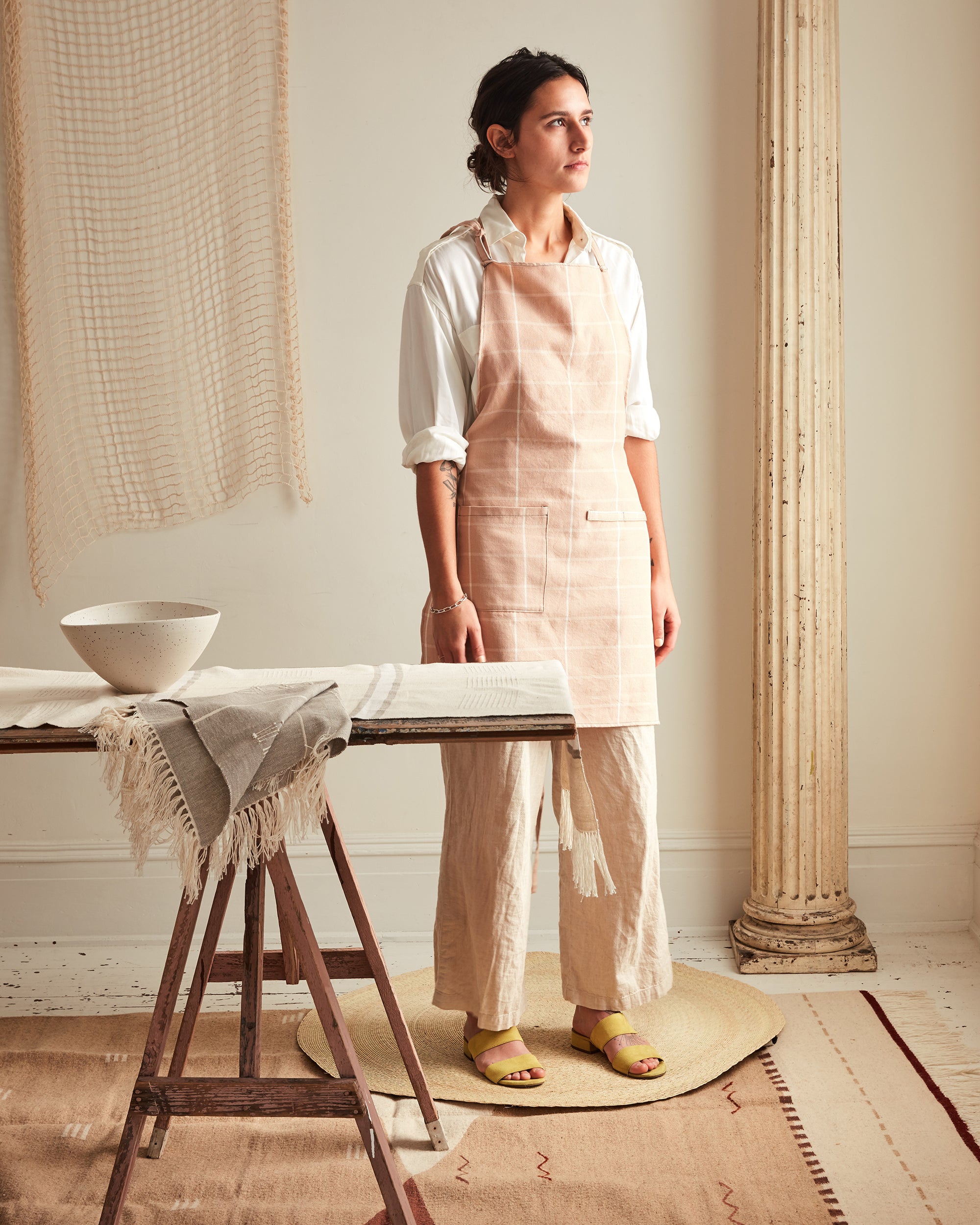 A person wears the ethically handwoven MINNA cotton kitchen apron in peach grid.