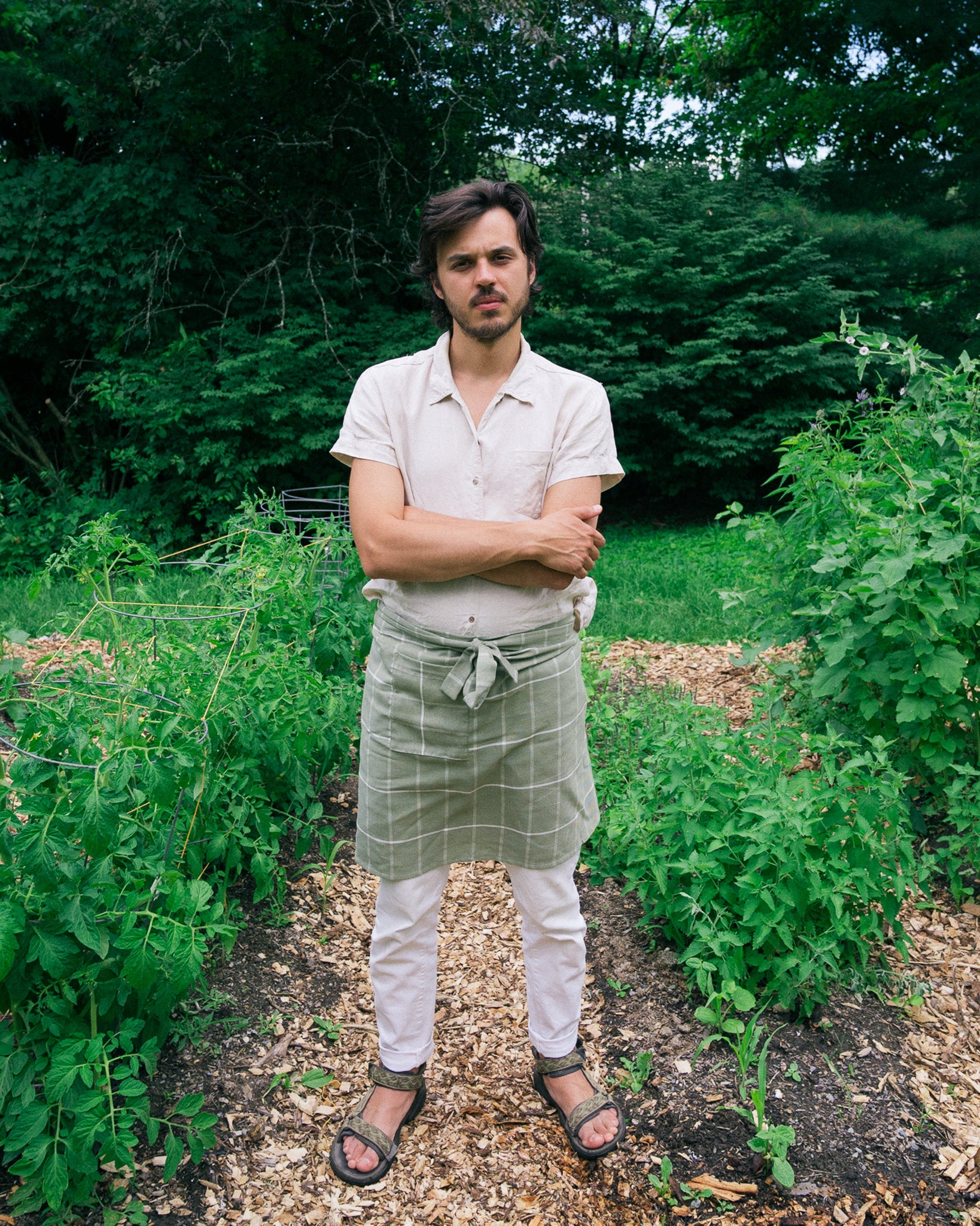 A person wearing the ethically handwoven cotton MINNA bistro apron in sage green.