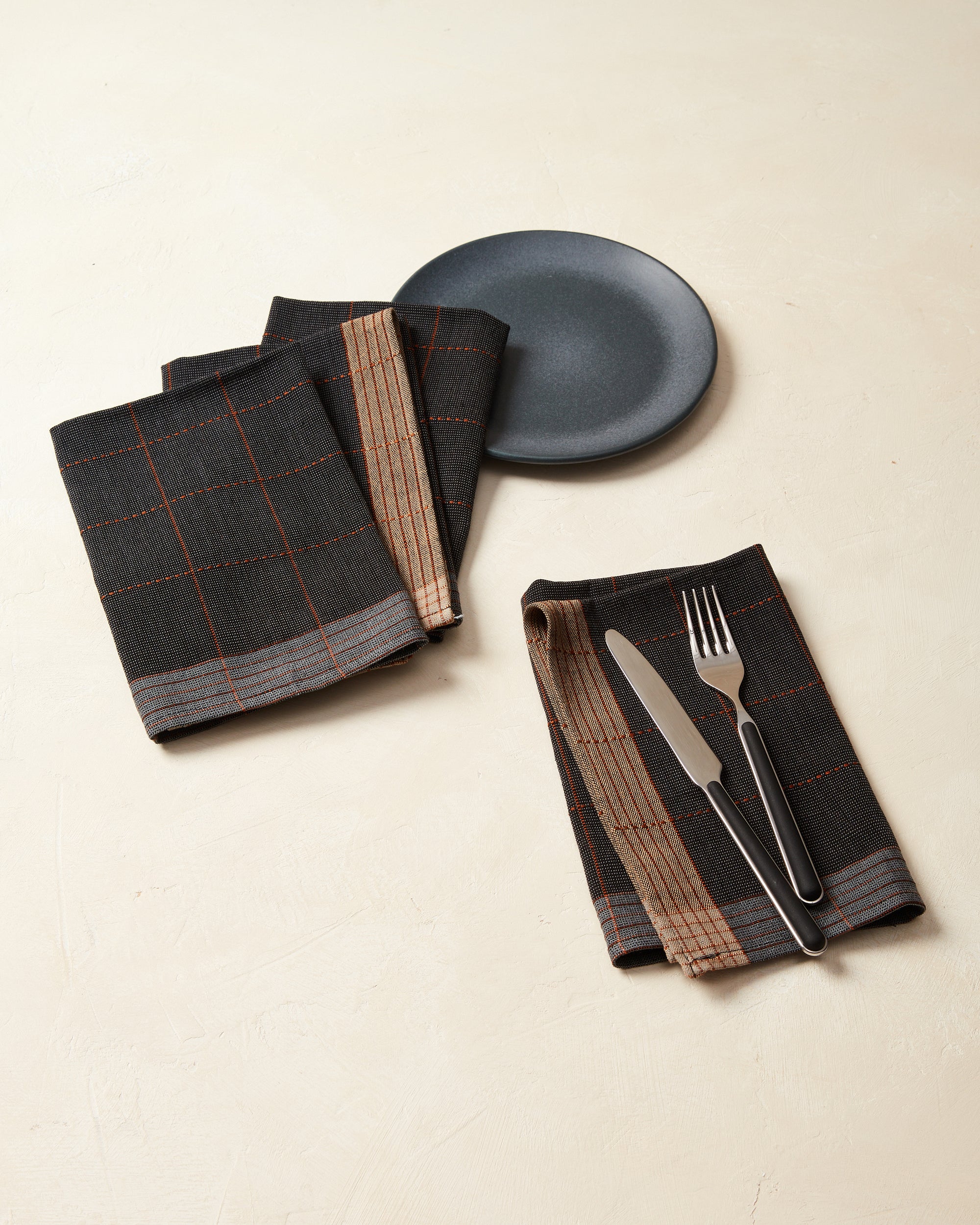 MINNA ethically handwoven cotton napkins in a grid pattern in black, charcoal, and brown.