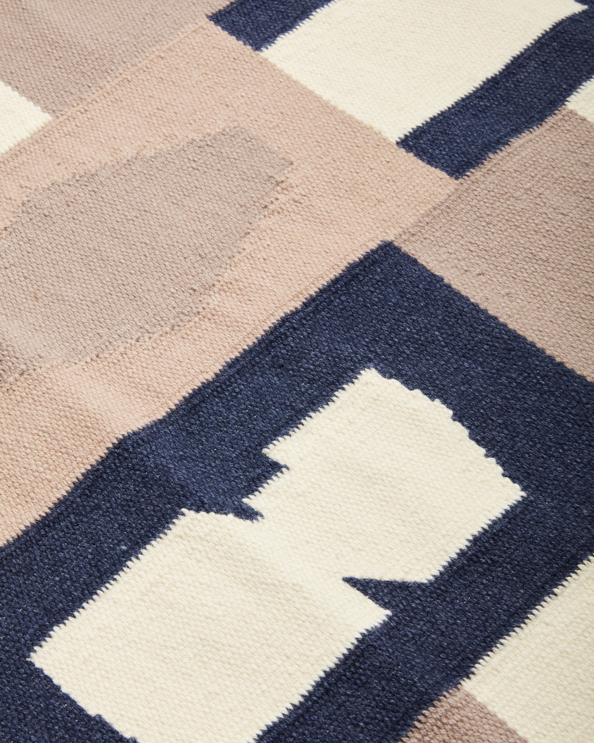 close-up of Vessels Rug Dune by MINNA. Handwoven wool flat weave rug in graphic pattern cream, beige, taupe, dark blue
